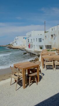 Relax at a charming cafe by the waves in Naousa, Paros, Greece. Enjoy breathtaking views of the sea and iconic white buildings while savoring local delicacies on a sunny day.