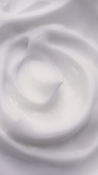 White Cream Swirling. Thick glossy cream moves in smooth folds, creating a soft abstract cosmetic texture.