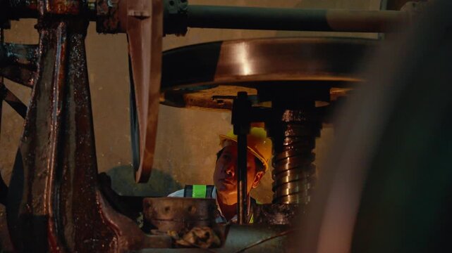 Engineer wearing safety equipment inspecting mechanical components of heavy industrial machinery inside a manufacturing workshop. Maintenance, engineering, and quality assurance concept.
