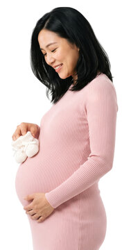 smiling pregnant asian woman in a pink dress holds small white baby shoes