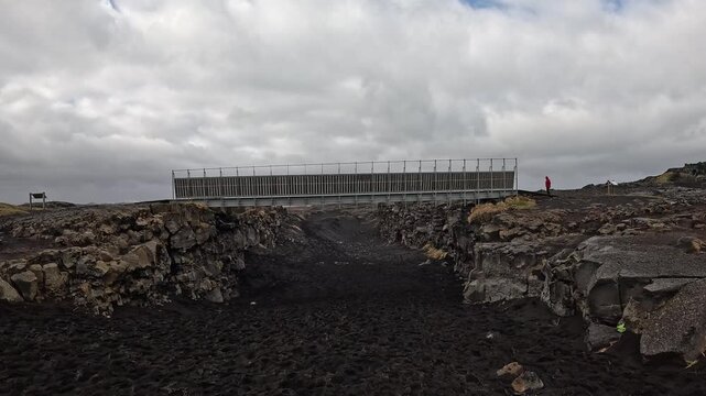 Approaching and walk under Bridge Between Continents spanning tectonic plate fissure from below, visitor on platform, Reykjanes, Iceland