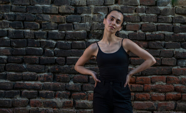 Portrait of beautiful young Hispanic woman in black tank top standing against brick wall and looking at camera.