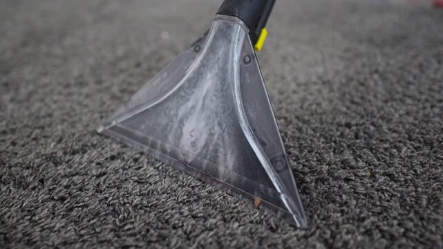 Clear triangular carpet extractor wand presses into dark textured carpet and pulls moisture and foam into nozzle, producing lighter cleaned path and visible wet sheen