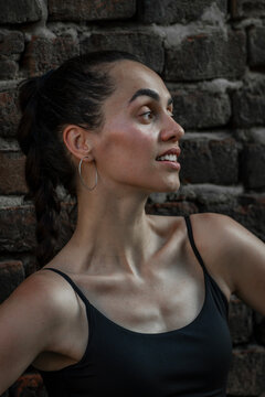 Close up beauty portrait of beautiful young Hispanic woman in semi-profile against brick wall.