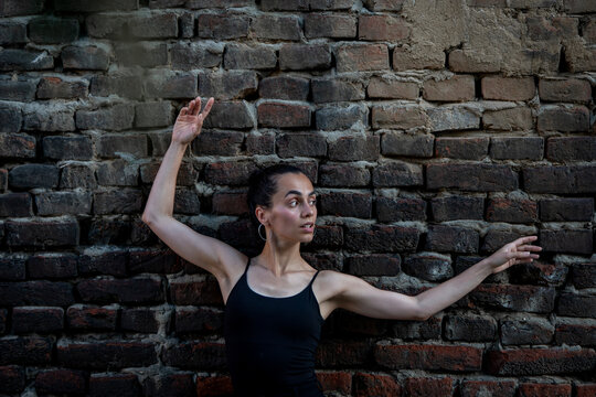 Beautiful young Hispanic woman practicing choreography poses against brick wall. Urban dancer concept.