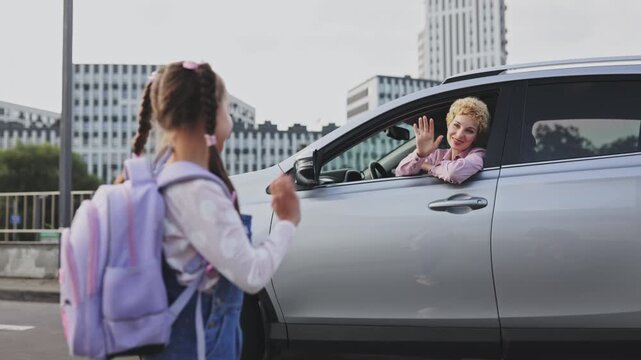A Caucasian mother waves goodbye to her daughter who is heading to school with her backpack