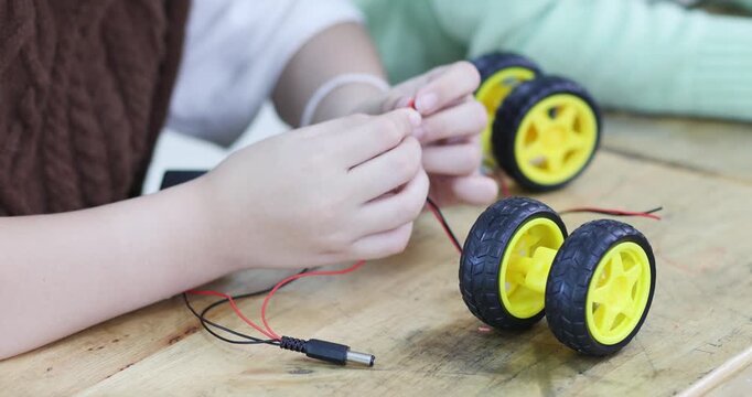 Elementary students assembling a robot car and connecting electronic wires in a STEM classroom. Hands-on learning, robotics, engineering, teamwork and back to school concept