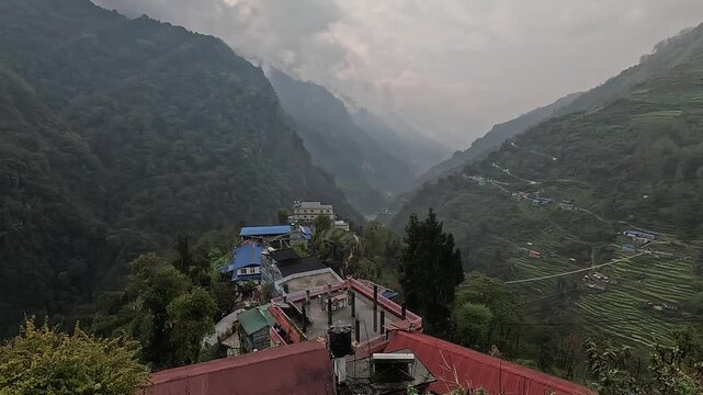 Tin rooftops of Jhinu Danda below forested ridges in a misty valley on the Annapurna Base Camp trek, Nepal