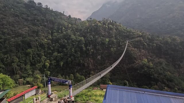 Elevated pan across the valley and the long Jhinu Danda suspension bridge between forested ridges, Annapurna trek, Nepal