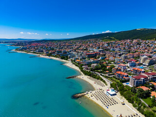 Fototapeta premium Coastal view of a city by the beach with clear water and green hills under a blue sky in the daytime