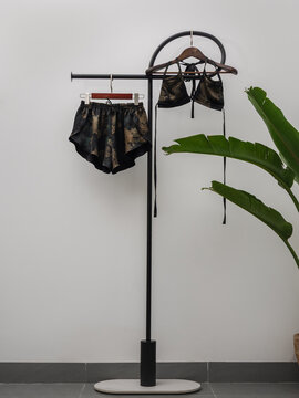 Patterned bikini and matching beach shorts hanging on minimalist clothing rack with tropical plant