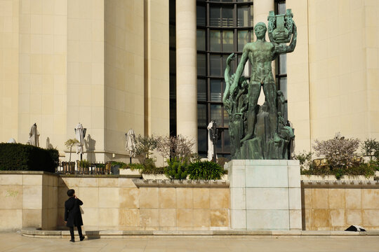 A man in a dark coat looking at the monumental bronze statue in Trocadero Square, Paris. 