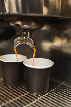 Espresso coffee machine pouring fresh hot coffee into two black paper cups.