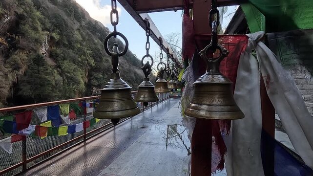 Row of brass ritual bells and prayer flags lining a footbridge, Annapurna region, Nepal