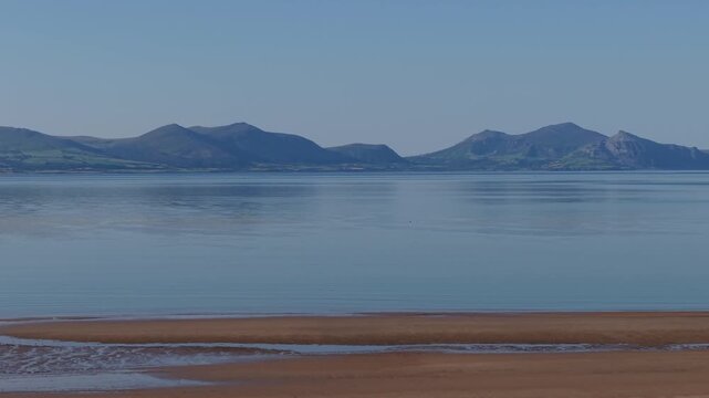 A drone flight on a hot early morning flying from Newborough beach over the Menai strait towards snowdonia.