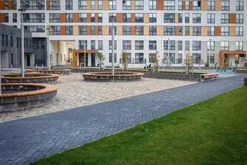 Courtyard plaza with paved pathway and round wooden benches near apartment buildings © seregraff
