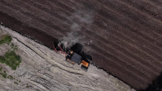 Drone shot of tractor ploughing farming field to prepare for Spring growing season and fertilizer application.