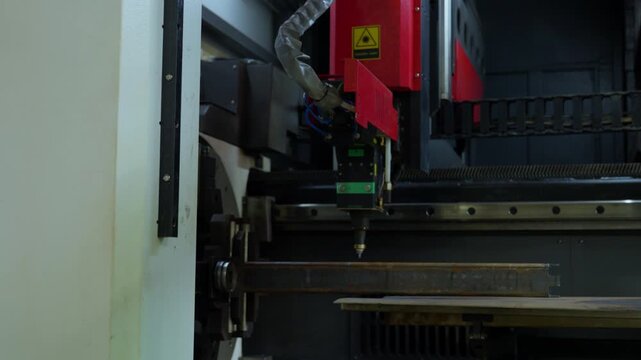 CNC laser cutting head trimming horizontal steel tube on red gantry with bright sparks and glowing cut point in dim workshop light during active fabrication, with laser, cutting, metal, tube detail
