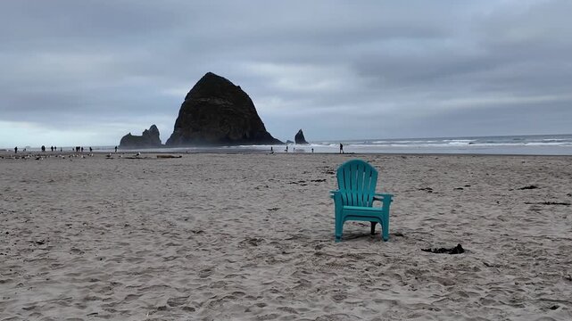 4K smooth stabilized footage of empty Adirondack chairs on Cannon Beach after Independence Day celebrations with Haystack Rock, Pacific Ocean and cloudy summer sunrise in Oregon, USA