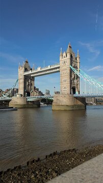 Wide vertical view of Tower Bridge with exposed foreshore at low tide beside the River Thames in London.