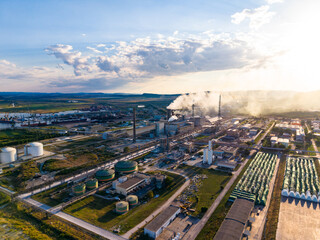 Fototapeta premium Factory complex located near a river with smoke rising from chimneys during sunset in an industrial area