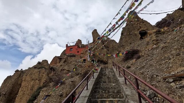 Pan view over staircase leading up to red mud walled Monastery with Prayer flags strung across eroded canyon cliffs at Shree Luri Gompa, Upper Mustang, Nepal