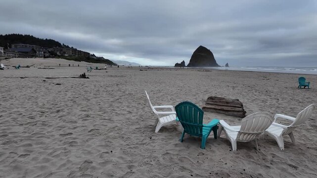 4K smooth stabilized footage of empty Adirondack chairs on Cannon Beach after Independence Day celebrations with Haystack Rock, Pacific Ocean and cloudy summer sunrise in Oregon, USA