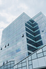 Obraz premium Modern office building with glass facade and unique architectural design in an urban setting under a cloudy sky
