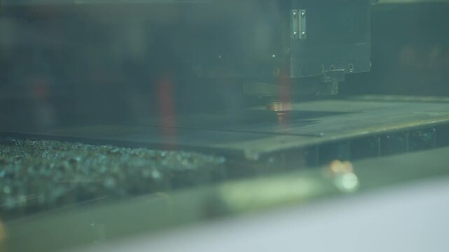 CNC laser cutting head producing bright sparks over flat steel plate in factory production area, precise industrial metal cutting with concentrated beam, glowing point and reflective support bed