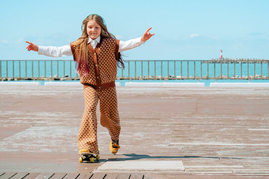 A happy girl skateboards on a sea embankment listening to music