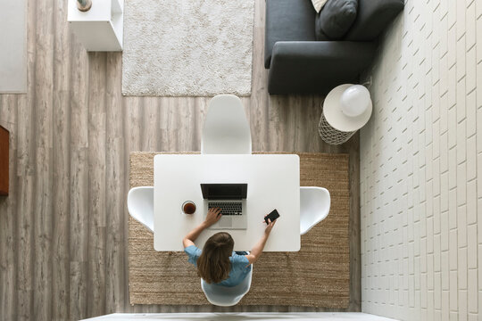 Woman sitting at table in modern loft using laptop and smartphone, top view