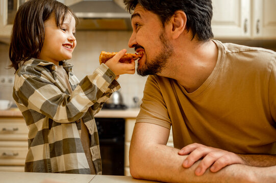 Happy boy feeding pizza to father at home