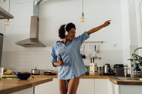 Woman dancing and listening music in the morning in her kitchen
