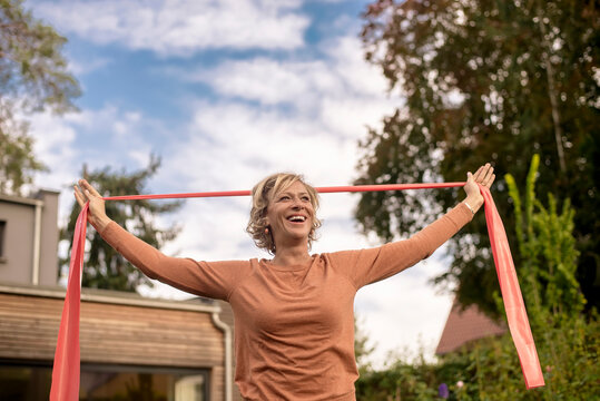 Smiling woman holding exercise band while standing at back yard