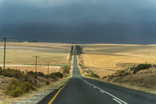 Endless road through dry fields under stormy sky in Swellendam
