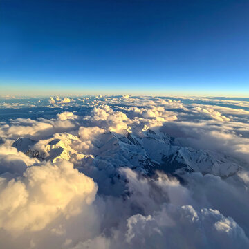 A majestic aerial view of snowcapped mountains soaring above golden sunrise clouds under a clear blue sky, evoking a feeling of freedom and wonder in a peaceful nature setting nobody.