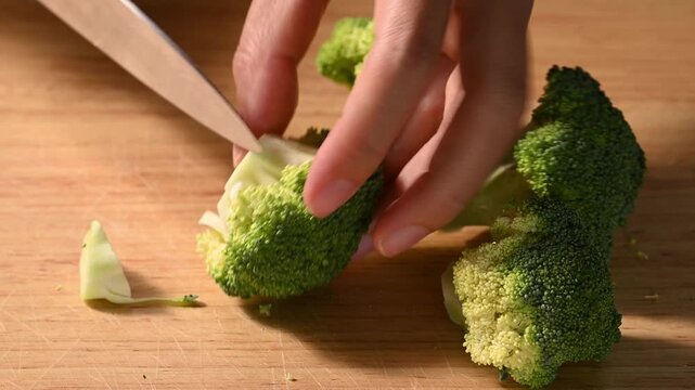 Close-up of woman hand using knife to chopping fresh broccoli on wooden cutting board, meal prep