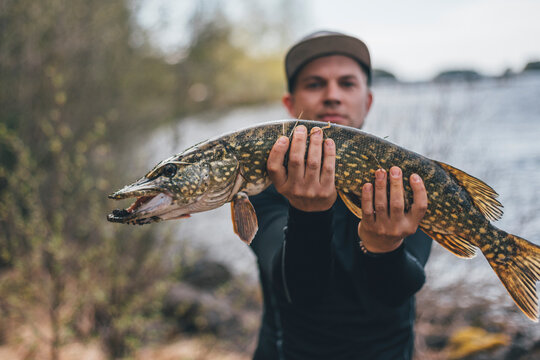 Young man holding proudly pike into camera