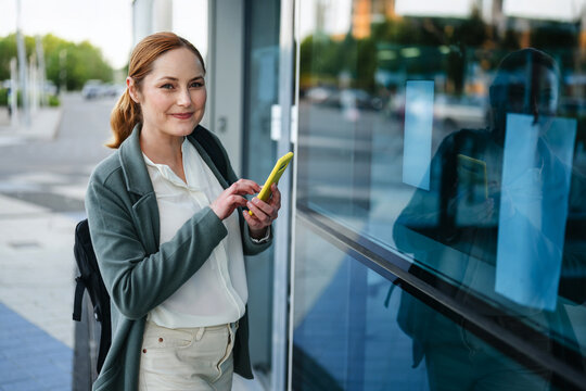 Smiling businesswoman waiting with smartphone outdoors in the city
