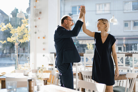 Successful businessman and woman high-fiving in a coffee shop