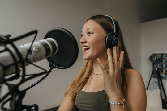 Close-up of happy teenage girl singing against wall in recording studio