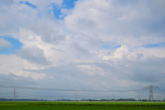 Power line crosses a green field under a cloudy sky in Groningen