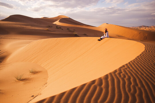 Young woman sitting on sand dune at Sahara desert in Morocco, Africa
