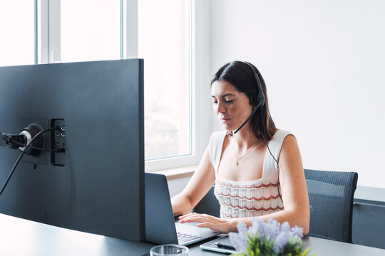 Young customer service representative with headset using laptop in office