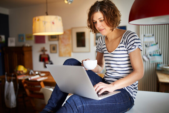 Portrait of mature woman sitting on kitchen table using laptop