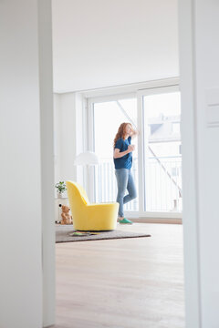 Young woman standing in her living room looking through window
