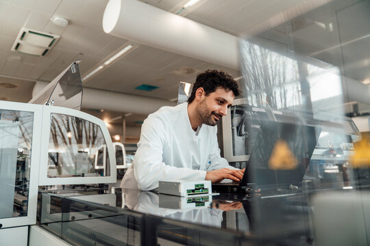 Smiling scientist analyzing data on laptop in modern laboratory