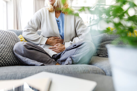 Woman having stomach ache sitting on sofa at home