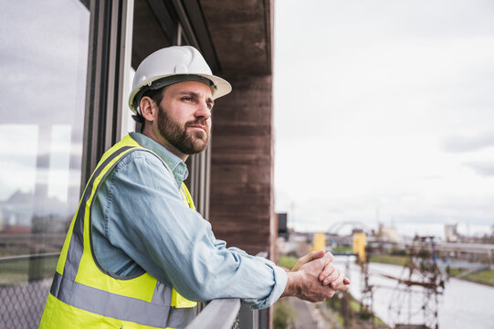 Contemplative building contractor leaning on railing