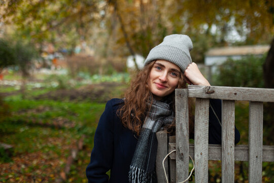 Cheerful woman in warm clothing leans on a wooden fence outdoors